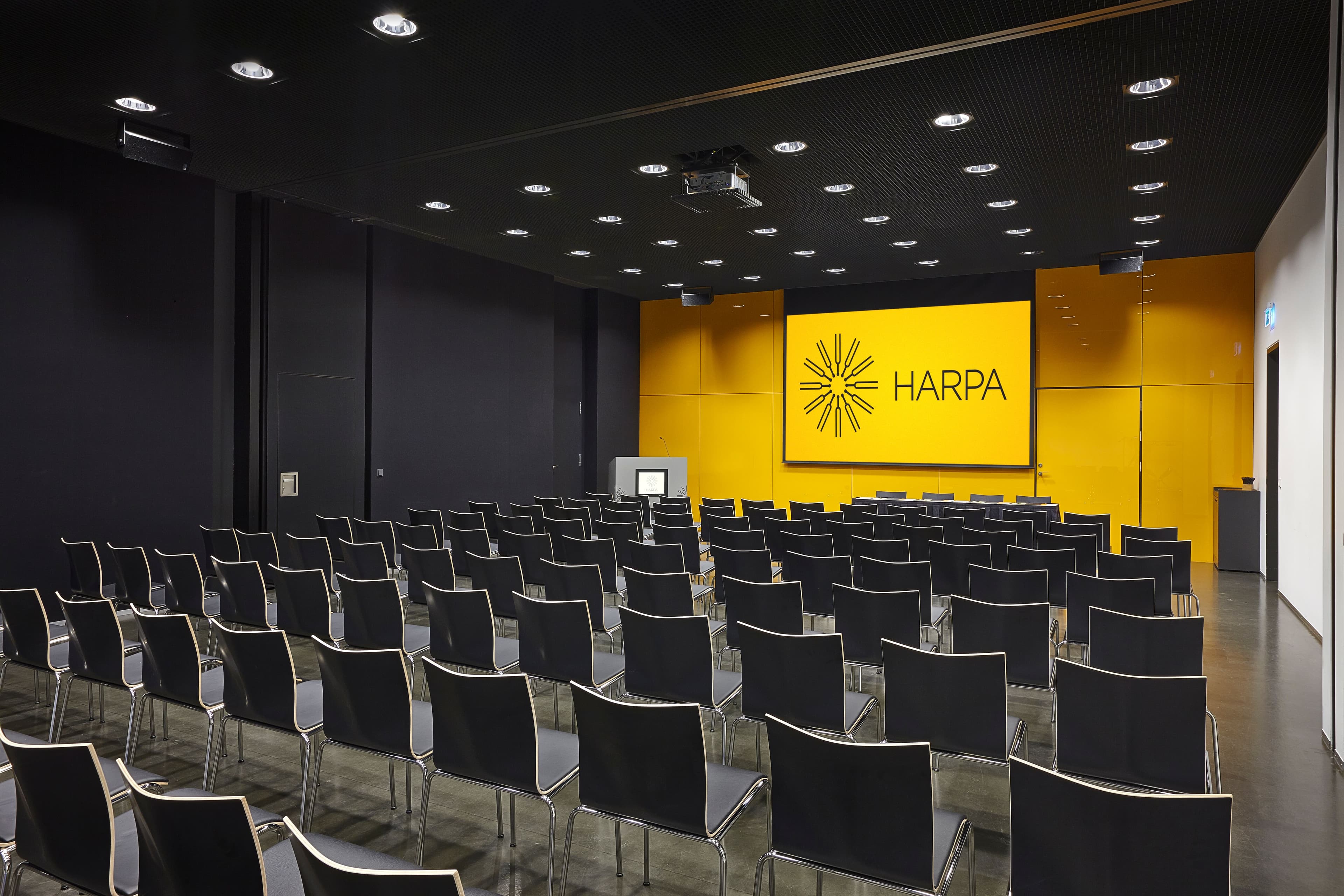 a large conference room with rows of black chairs and a large screen .