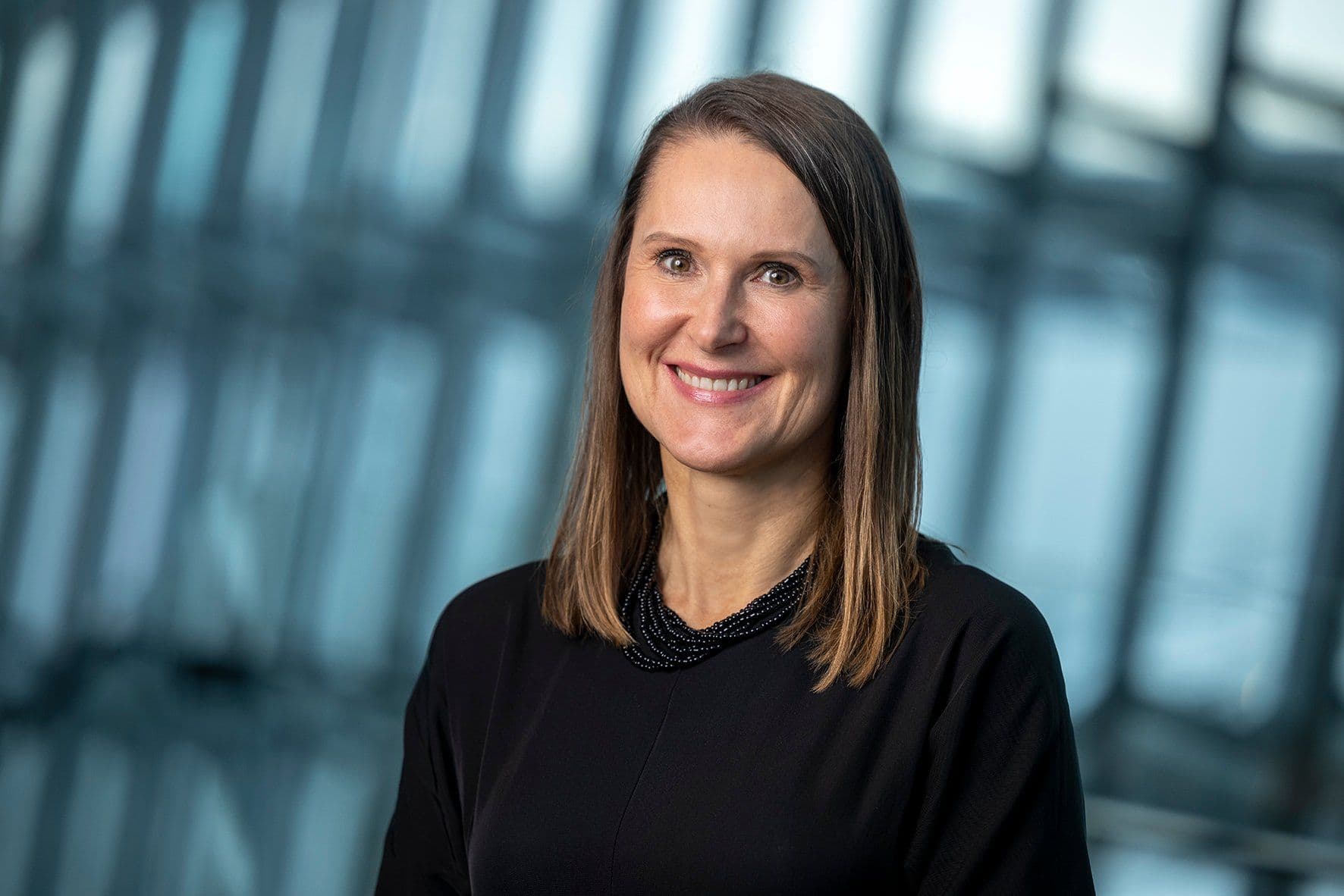 a woman in a black dress and necklace is smiling for the camera .